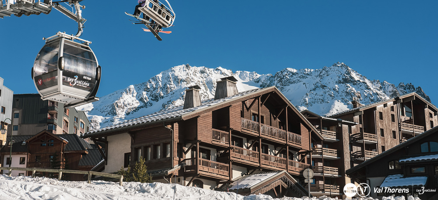 Résidence L’Oxalys’ timber chalet buildings in Val Thorens, with a gondola passing overhead